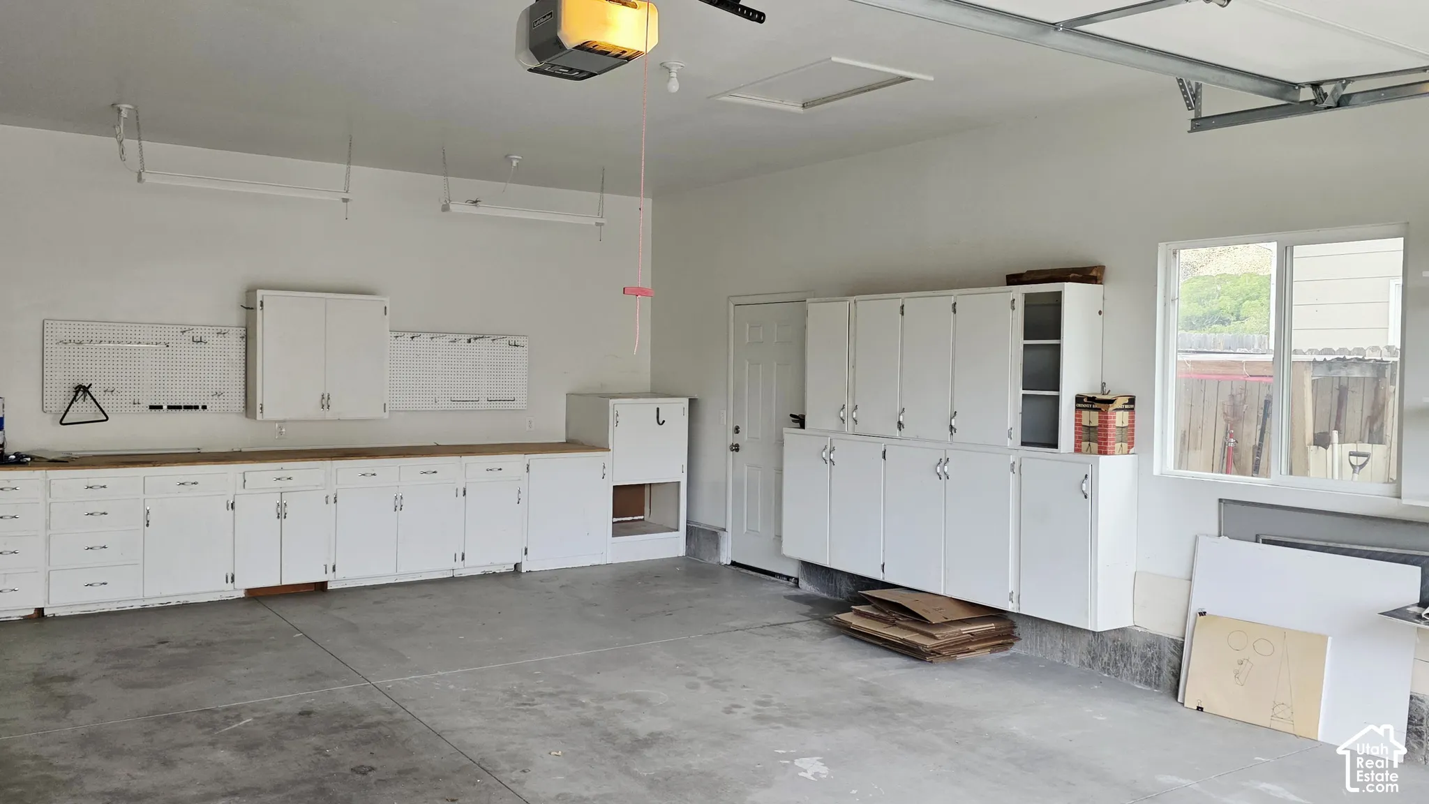 Garage featuring extensive white built-in cabinetry, dual wall-mounted storage configurations, concrete flooring, and an integrated overhead garage door opener