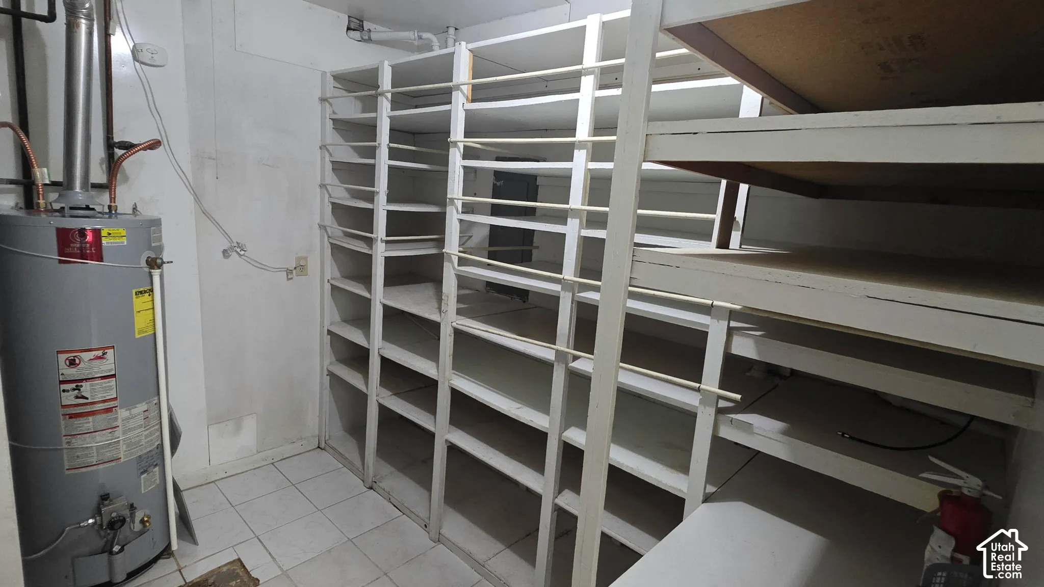 Storage room featuring white built-in shelving, tile flooring, and a water heater