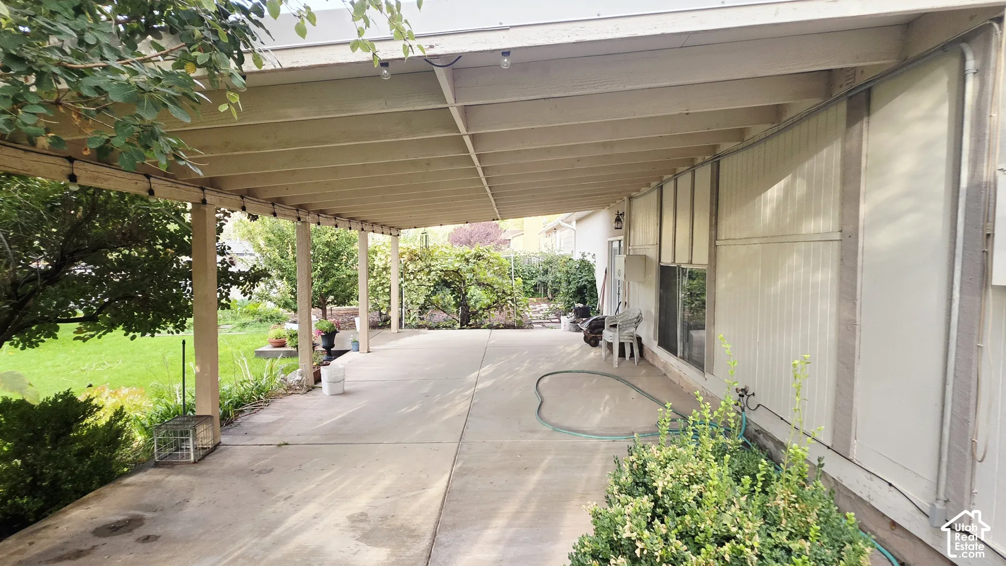Covered concrete patio featuring an exposed beam ceiling, exterior wall-mounted lighting, and integrated support posts