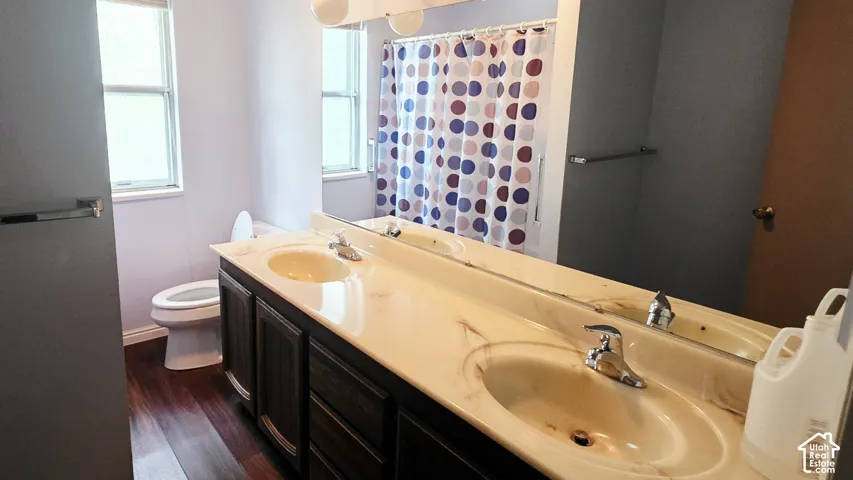 Double vanity with integrated sink basins, laminate countertop, dark wood-finish cabinetry, full-width mirror, and wood-finish flooring