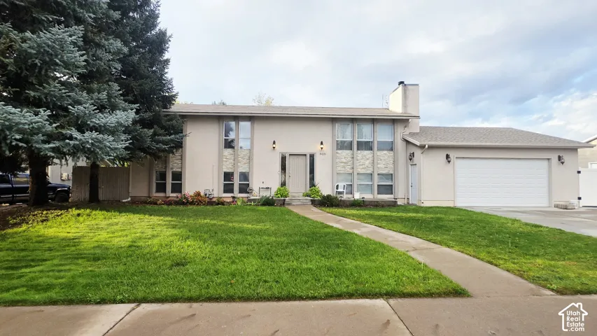 Multi-level exterior featuring light-toned stucco siding, stone veneer accents, multi-pane vertical windows, an attached two-car garage, and concrete walkway