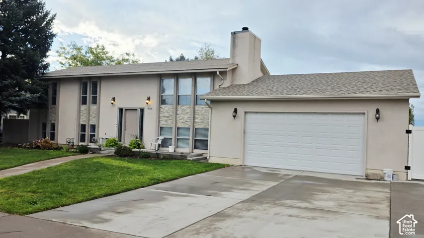Stucco exterior featuring stacked stone accents, a multi-paneled garage door, expansive front windows, and an exterior chimney