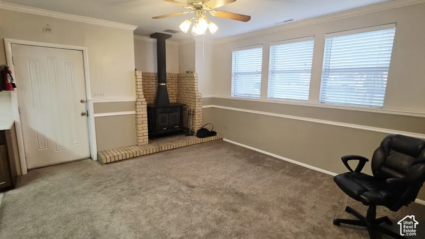 Freestanding wood-burning stove with a brick hearth, carpeted flooring, crown molding, chair rail, and horizontal window blinds