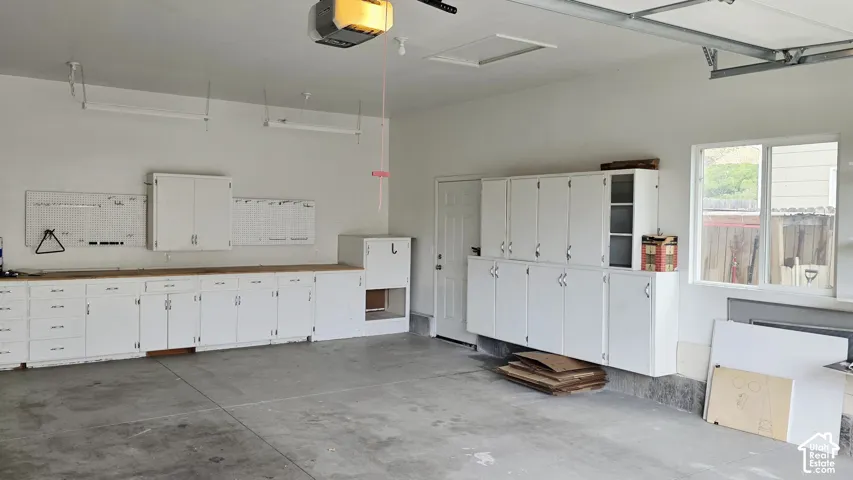Garage featuring extensive white built-in cabinetry, dual wall-mounted storage configurations, concrete flooring, and an integrated overhead garage door opener