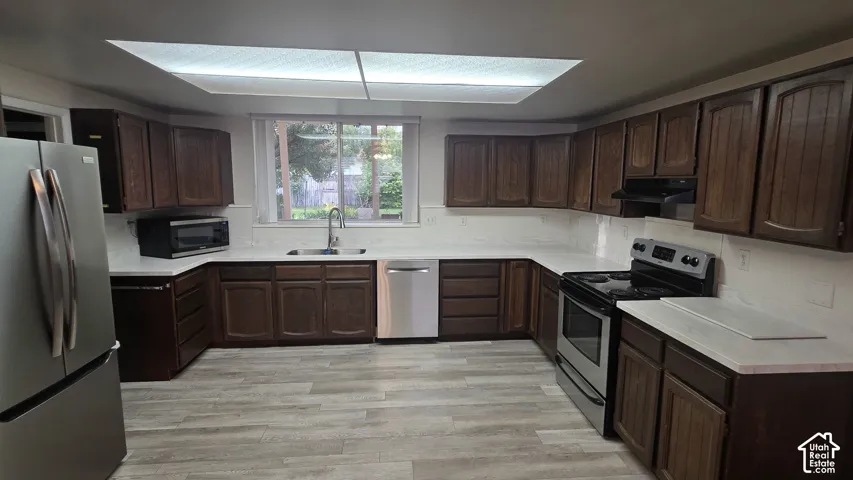 Kitchen featuring dark wood cabinetry, light countertops, stainless steel appliances, and wood-finish flooring