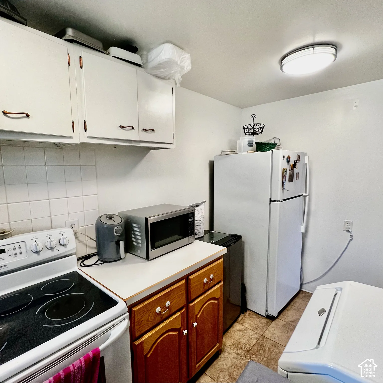 White upper cabinetry with contrasting wood-finish base cabinets, white tile backsplash, and a built-in range
