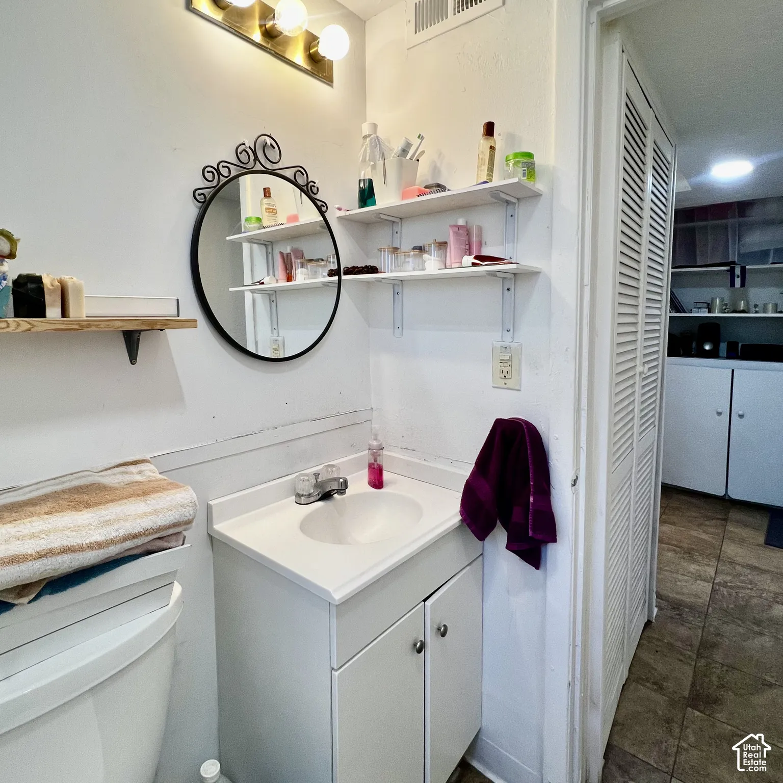 Vanity with integrated sink, wall-mounted shelving, and overhead lighting