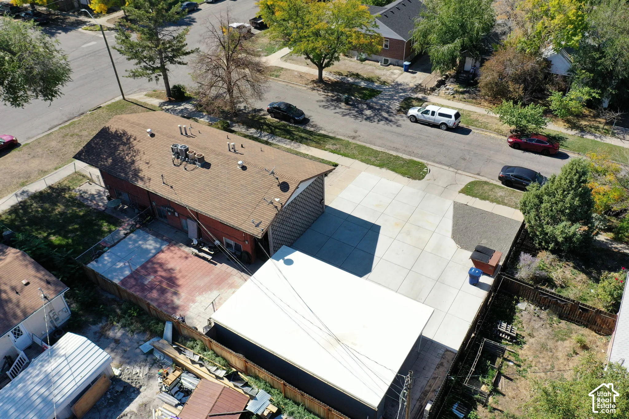 Aerial perspective featuring a large concrete parking area, a detached garage with a white flat roof, a paved patio, and perimeter fencing