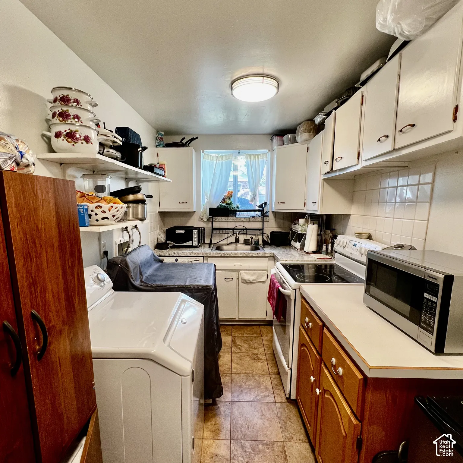 Galley-style kitchen featuring white upper cabinetry, lower wood-finish cabinetry, tile backsplash, laminate countertops, and tile flooring