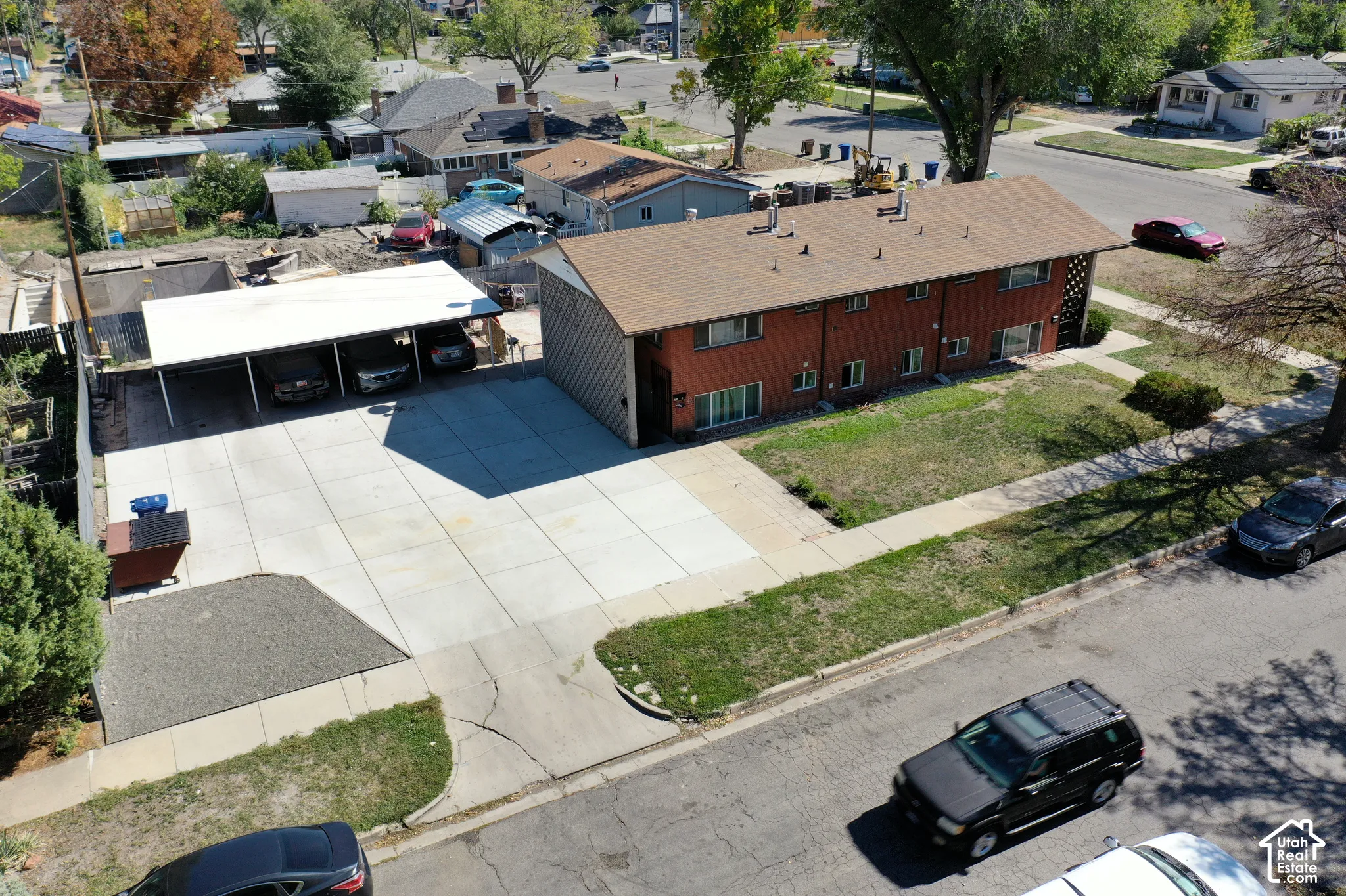 Multi-unit property featuring a brick exterior, shingle roof, concrete parking pad, and covered carport structure