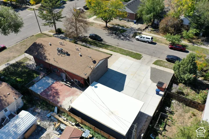 Aerial perspective featuring a large concrete parking area, a detached garage with a white flat roof, a paved patio, and perimeter fencing