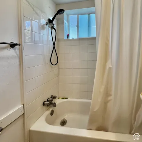 Bathtub with an integrated shower, white tiled surround, and a frosted window