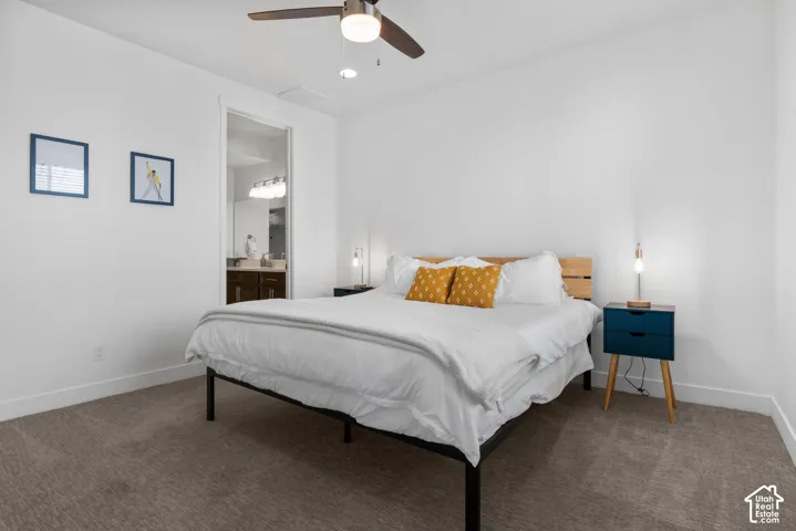 Neutral wall finishes, plush carpeting, ceiling fan with integrated lighting, and a doorway revealing a vanity with an illuminated multi-bulb fixture
