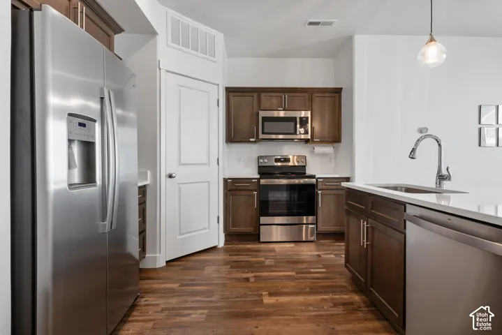 Kitchen featuring dark wood cabinetry, stainless steel appliances, light-toned stone countertops, and wood-finish flooring