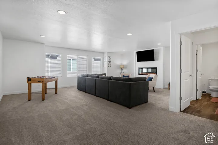 Open-concept interior featuring recessed lighting, carpeted flooring, a white brick-finish accent wall, and a built-in electric fireplace