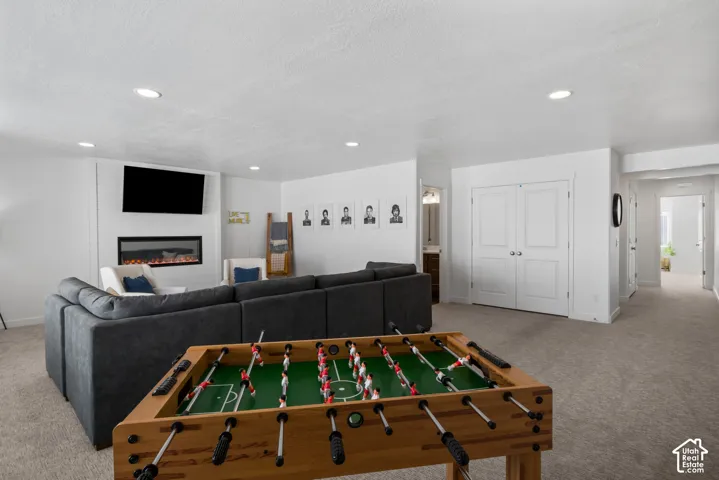 Electric fireplace with a shiplap surround, wall-mounted television, recessed lighting, neutral carpeted flooring, and double-door storage closet