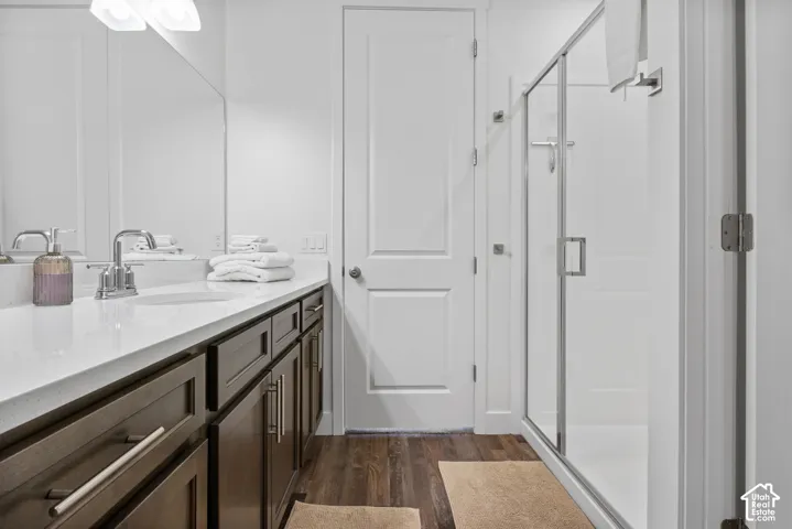 Bathroom featuring a wood-finish vanity with a stone-surface countertop, an integrated sink, full-width mirror, and a glass-enclosed shower with white surround panels