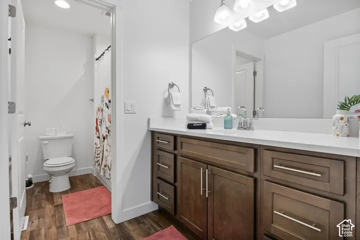 Bathroom featuring dark wood-finish cabinetry, a white countertop with an integrated sink, brushed-nickel hardware, wood-finish flooring, and a full-width vanity mirror with integrated lighting