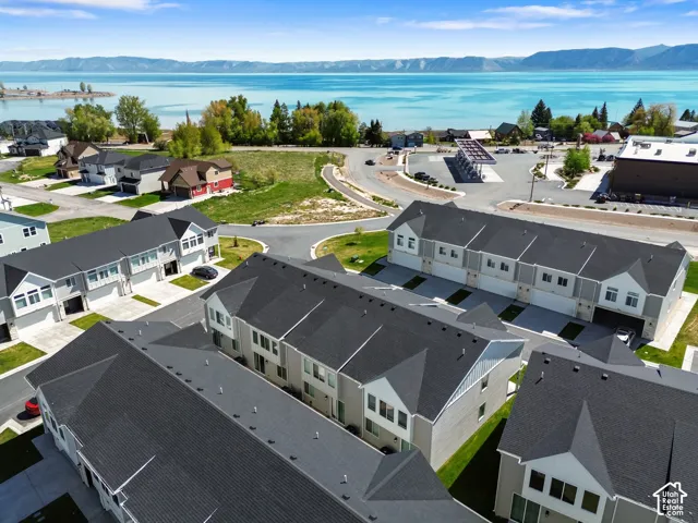 Multi-level residential structures featuring shingled roofs, integrated garages, and siding exteriors, positioned near a large body of water and mountain backdrop