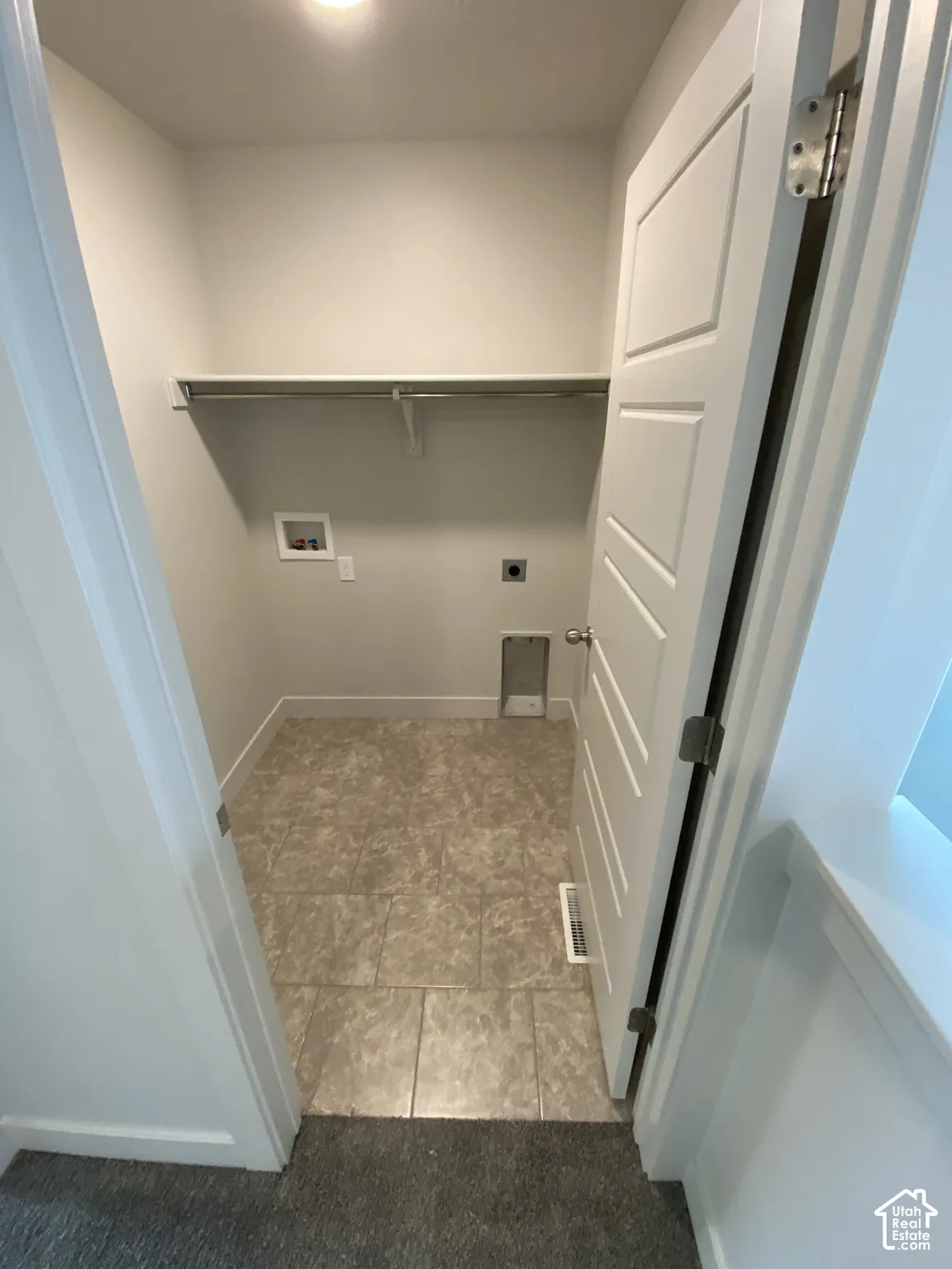 Dedicated utility area featuring tile flooring, a wall-mounted shelving unit with a metal hanging rod, and a five-panel interior door