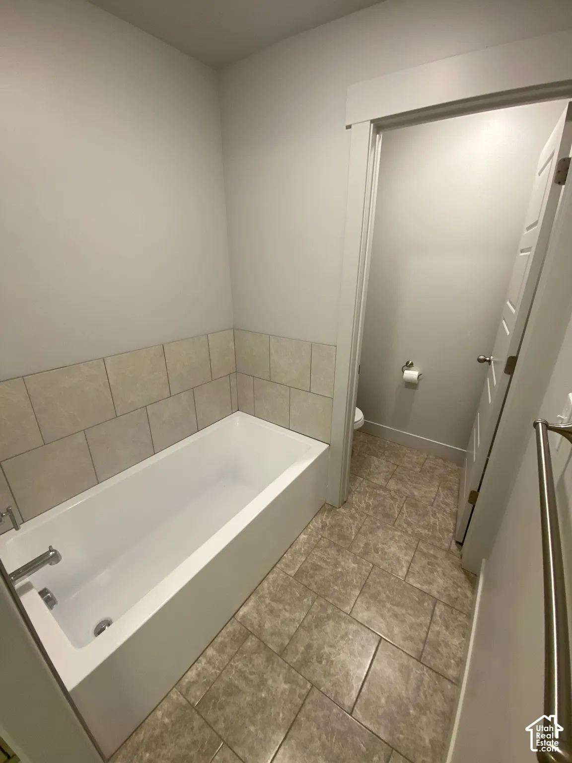 Bathtub with a neutral tile surround, large-format stone-pattern tile flooring, and metal towel bar