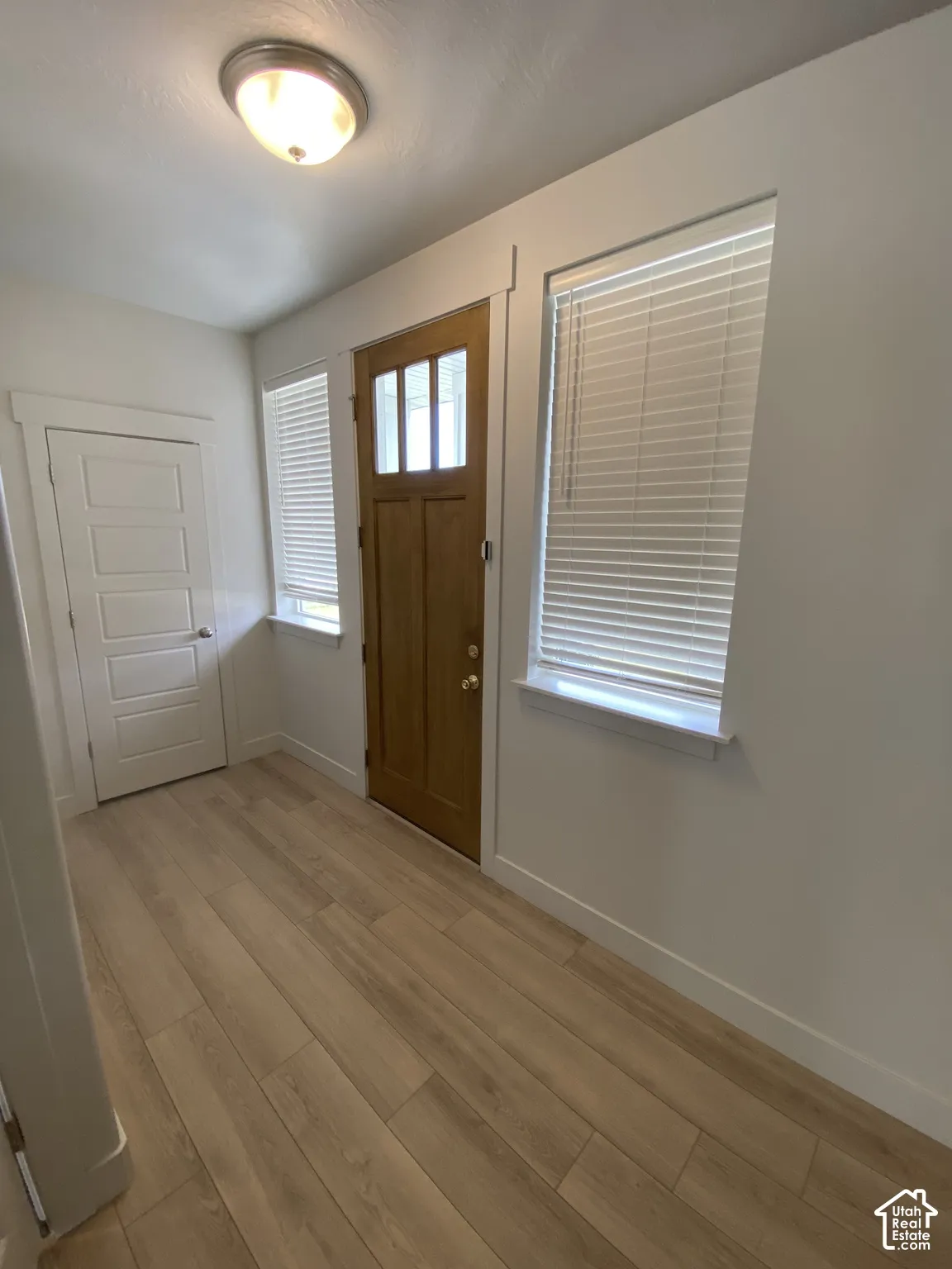 Entryway featuring a wood-finish entry door with a glass lite, wood-finish flooring, and two windows with horizontal blinds