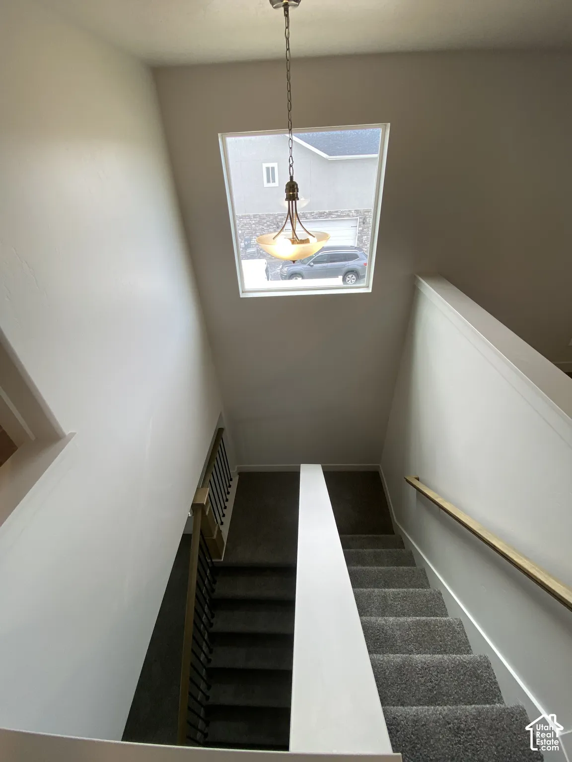 Staircase featuring carpeted steps, a wall-mounted wooden handrail, and a decorative pendant light fixture suspended before a large square window