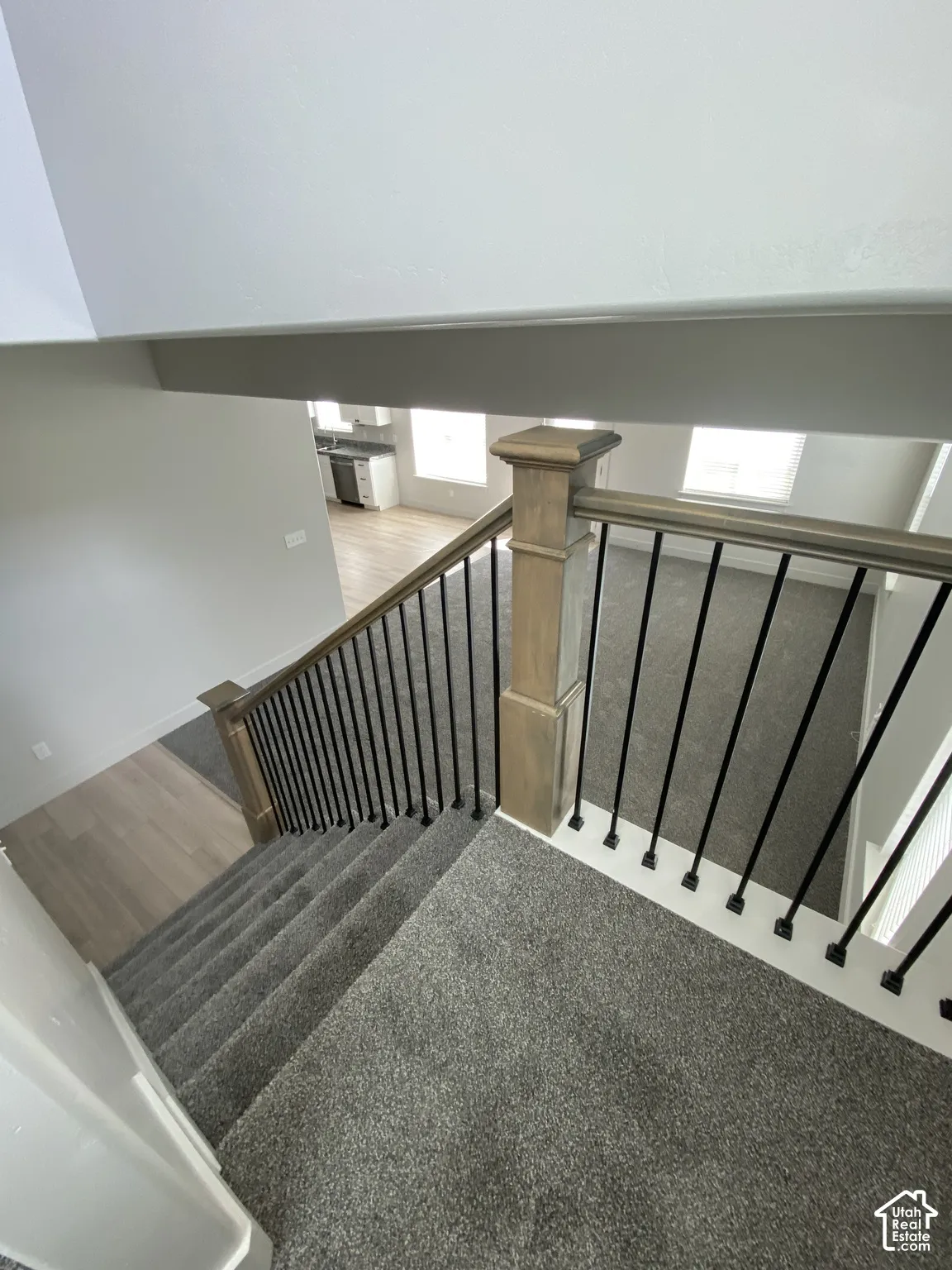 Staircase featuring dark carpeted treads, wood-finish newel posts, and metal balusters