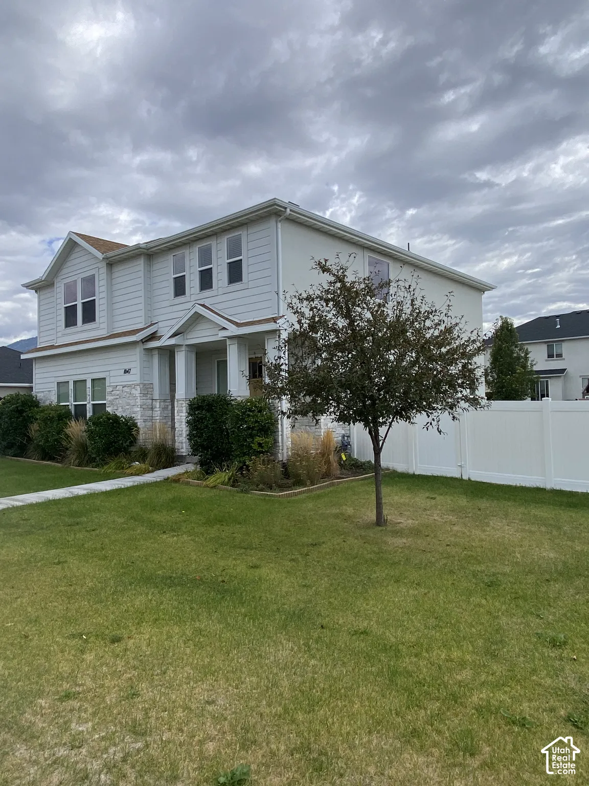 Two-story residence featuring light-colored horizontal siding, stone veneer accents, a covered front entryway, and a perimeter vinyl fence