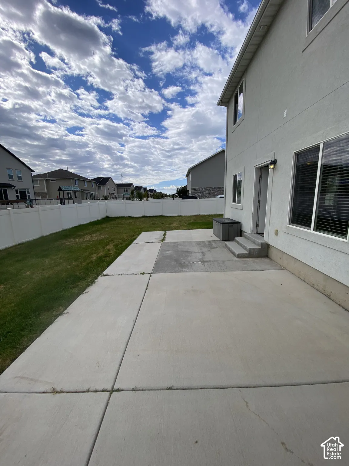 Rear exterior featuring a concrete patio, white vinyl privacy fencing, and a grass lawn