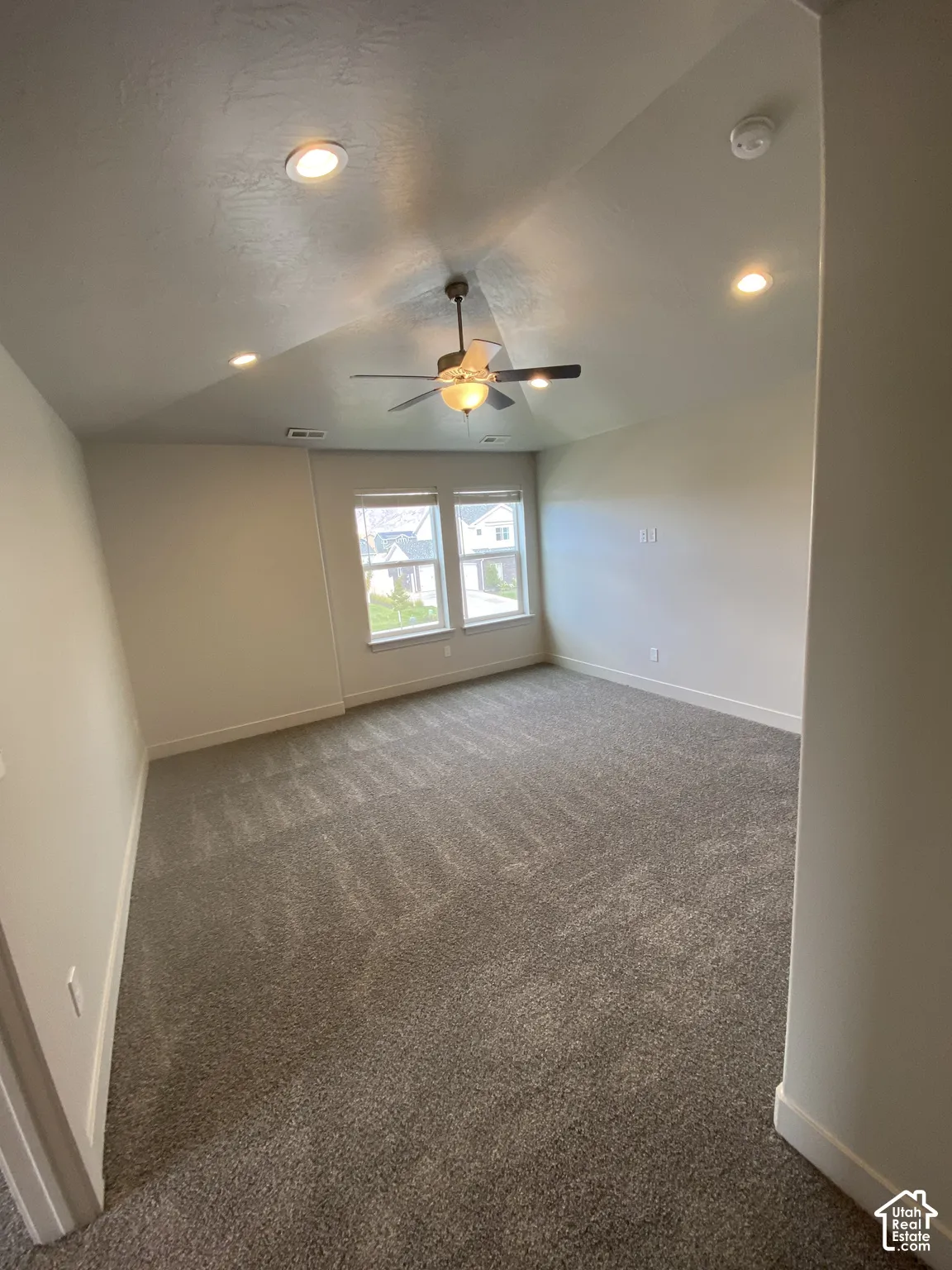 Vaulted ceiling with integrated recessed lighting and a central ceiling fan, neutral carpeting, and dual-pane windows