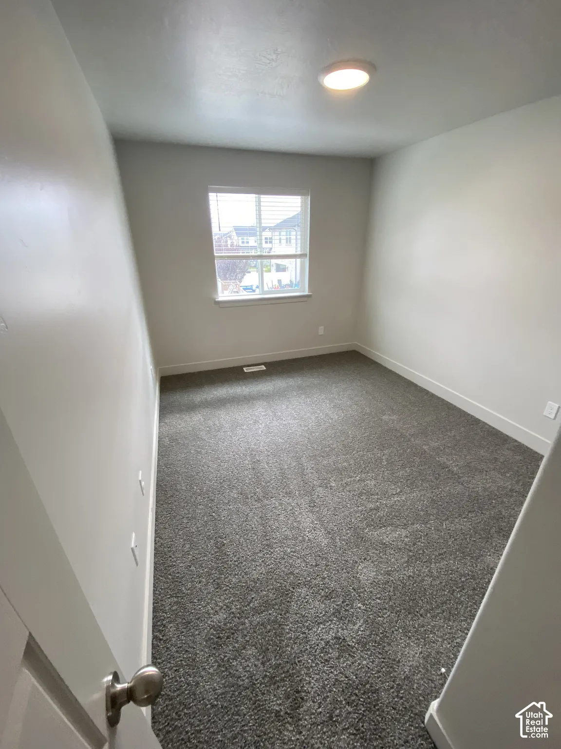 Neutral-toned room featuring neutral wall-to-wall carpeting, a single-pane window with white trim, and a ceiling-mounted flush mount light fixture