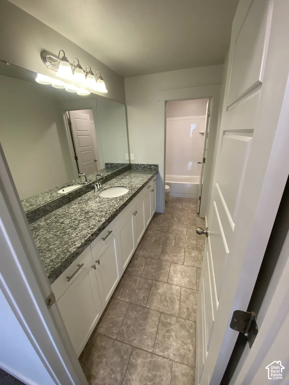 Dual vanity with stone-finish countertop, white cabinetry, integrated sink, full-width mirror, and tile flooring
