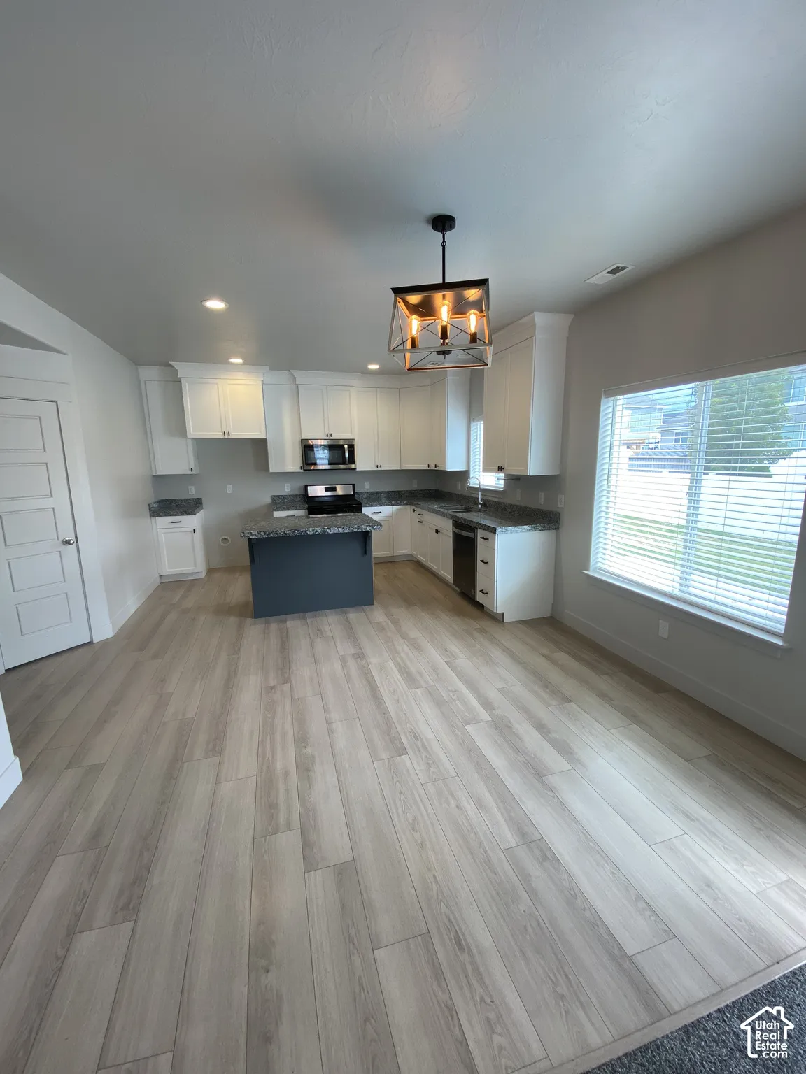 Kitchen featuring white shaker-style cabinetry, a dark-toned center island, stone-finish countertops, wood-finish flooring, and a metal-frame pendant light fixture
