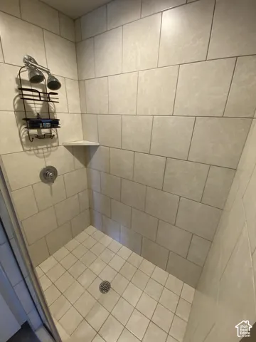Walk-in shower featuring large-format ceramic wall tiling in a running bond pattern, square floor tile, a built-in corner shelf, and a circular chrome shower control valve