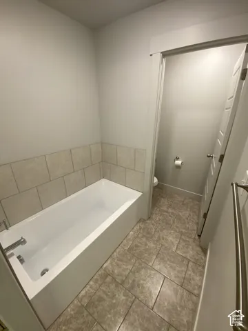 Bathtub with a neutral tile surround, large-format stone-pattern tile flooring, and metal towel bar