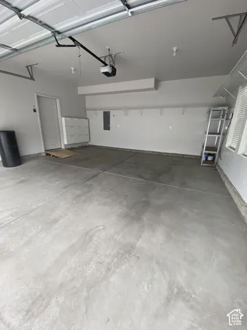 Attached garage featuring a concrete floor, built-in wall shelving, automatic garage door opener, and a dedicated service door