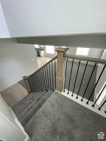 Staircase featuring dark carpeted treads, wood-finish newel posts, and metal balusters