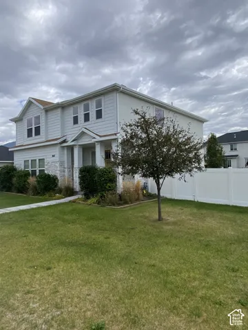 Two-story residence featuring light-colored horizontal siding, stone veneer accents, a covered front entryway, and a perimeter vinyl fence