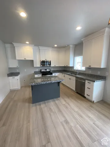 Kitchen featuring white shaker-style cabinetry, an island with a contrasting dark base, stone-patterned countertops, stainless steel appliances, and wood-finish flooring