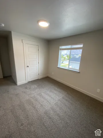 Neutral-toned interior room featuring wall-to-wall carpeting, a multi-panel interior door, a flush-mount ceiling light fixture, and a large window with exterior mountain scenery