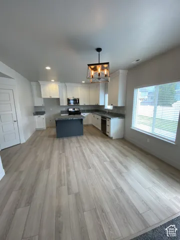Kitchen featuring white shaker-style cabinetry, a dark-toned center island, stone-finish countertops, wood-finish flooring, and a metal-frame pendant light fixture