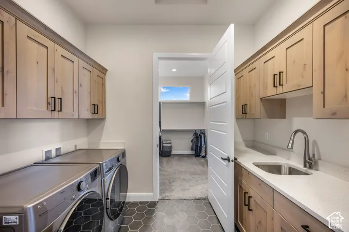 Laundry room featuring light wood-finish cabinetry, stone-composite countertops, integrated stainless steel sink with high-arc faucet, and dark hexagonal floor tiling