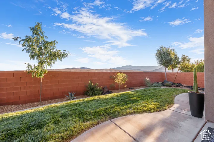 Backyard featuring a concrete patio, sod lawn, perimeter masonry wall, and desert-adapted plantings with mountain scenery