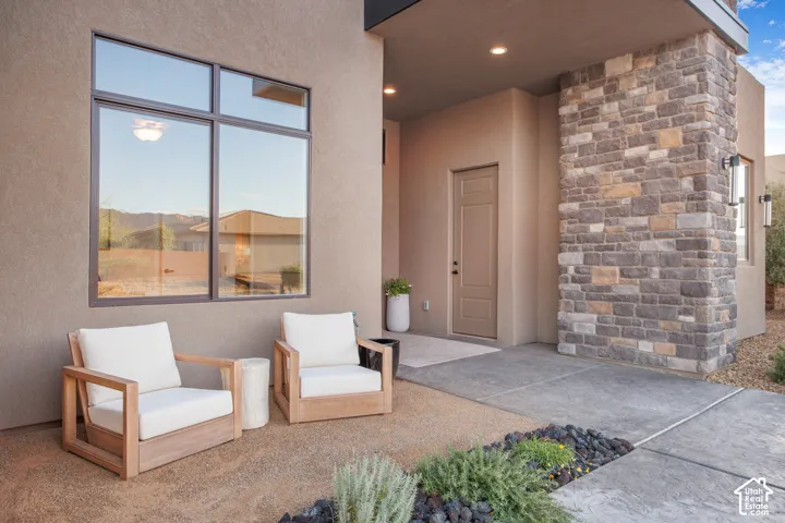 Contemporary exterior featuring a textured stucco facade, stone masonry pillar, recessed ceiling lighting, and expansive multi-pane windows