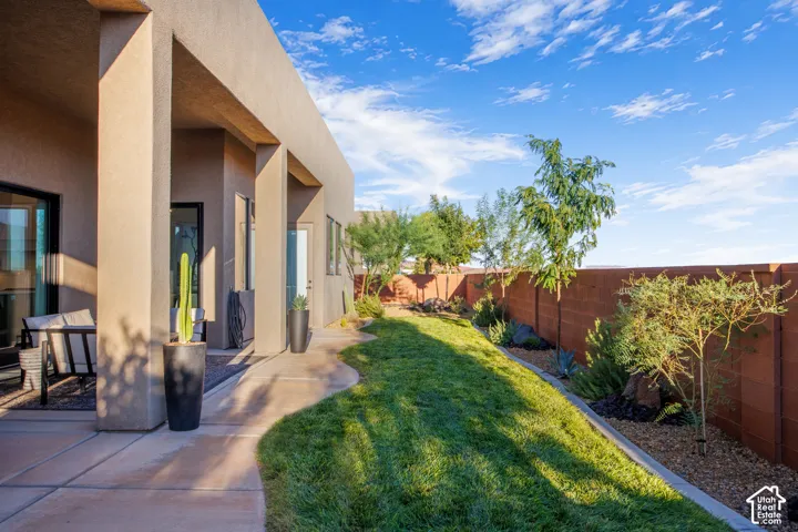 Covered patio featuring a smooth-finish concrete floor, natural grass lawn, mature landscaping, and a masonry perimeter wall