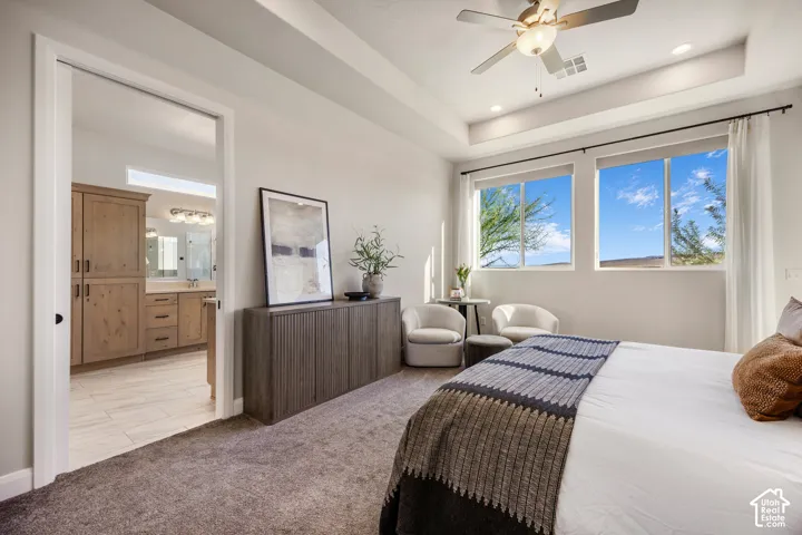 Bedroom featuring a tray ceiling, ceiling fan with integrated lighting, neutral wall-to-wall carpeting, and large dual windows