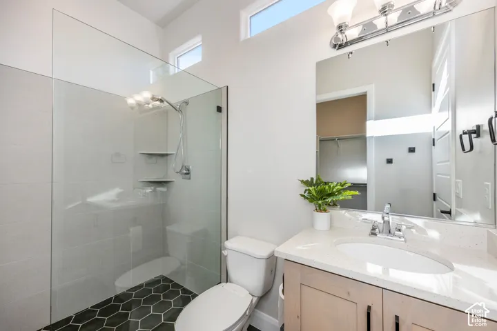 Bathroom featuring a walk-in shower with glass enclosure, light-toned cabinetry, light-colored stone-surfaced countertop, and dark-toned hexagonal floor tile