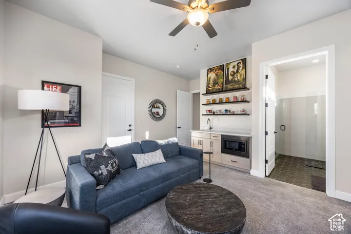 Built-in kitchenette featuring light wood cabinetry, white countertop, integrated microwave, and floating shelves, complemented by a ceiling fan