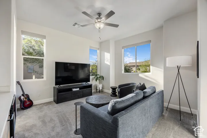 Neutral wall tones, carpeting, and triple-window configuration with a central ceiling fan and light fixture